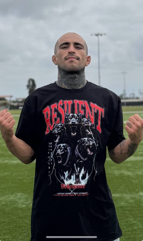 Person wearing a black t-shirt with graphic design and text outdoors on a grassy field.